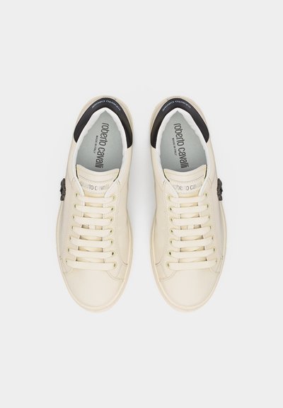 Paire de baskets en cuir écru avec lacets, accents noirs au talon, et inscription "Roberto Cavalli Made in Italy" à l'intérieur.