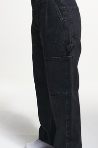 Black cargo pants with pockets, loose fit, and sturdy denim material. Features visible stitching and a loop detail on the waistband.