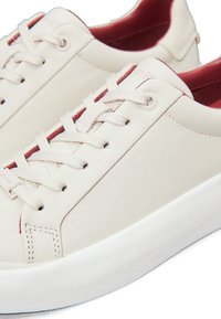 Hvide lædersneakers med en tekstureret overflade, prydet med beige snørebånd, en rød accent indeni og en hvid gummisål.