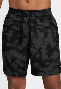 Svarta simshorts med ett abstrakt mörkt mönster, elastisk midja med dragsko och en liten vit Nike-logotyp längst ner till höger.