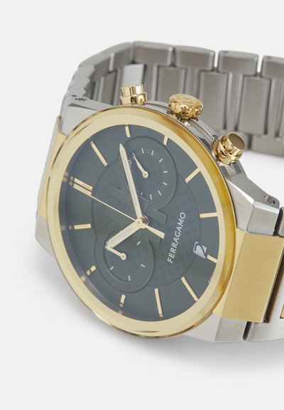 Gold and silver watch with a black patterned dial, three sub-dials, and a date window. Features a metal bracelet and push-button crowns.