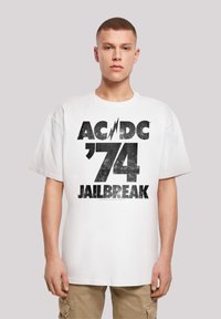 White oversized t-shirt made of cotton featuring a black graphic print with “AC/DC ’74 JAILBREAK” in a distressed style.