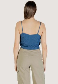 Canotta in denim con spalline sottili, caratterizzata da una forma aderente e un colore blu uniforme. Abbinata a pantaloni cargo color khaki su uno sfondo semplice.