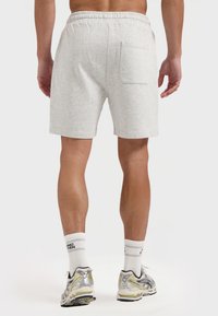 Grijze katoenen shorts met een elastische tailleband, een achterzak en een relaxte pasvorm, gecombineerd met witte sokken en lichtgekleurde sportschoenen.