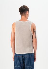 Top sin mangas de canalé beige con un ajuste relajado, que presenta un escote redondo y una textura lisa. El modelo se muestra de espaldas.