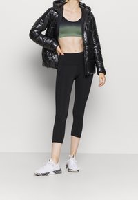 Svart puffjacka, grön ombre sport-bh och svarta leggings med kort passform, tillsammans med vita sneakers med ett mönstrat sula.