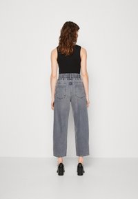 Pantalones de mezclilla gris de pierna ancha con una cinturilla fruncida y dos bolsillos traseros. Llevados con una blusa negra sin mangas y zapatos de plataforma negros.