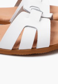 Sandali bianchi con ampie cinghie in materiale sintetico liscio, soletta imbottita color sabbia e suola in gomma marrone per una buona aderenza.