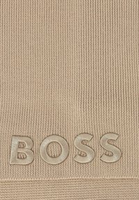 Tissu en maille beige avec des côtes verticales, présentant des lettres surélevées et en relief épelant "BOSS" dans une couleur assortie.