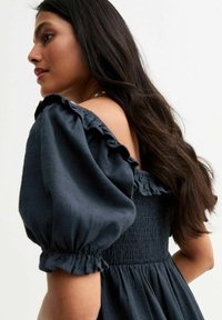 Vestido azul oscuro de mangas abullonadas con hombros con volantes y un cuerpo fruncido. La suave tela de algodón cae de manera suave, mostrando una cintura ajustada.