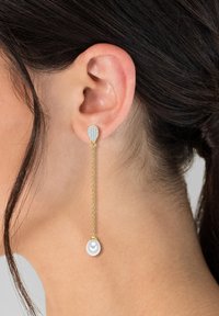 Gouden oorbellen met een druppelvormige kristallen stud en een hangende witte parel. Het ontwerp is strak met een moderne, elegante uitstraling.