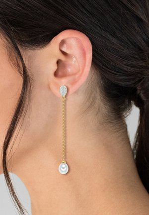 Guld kædeøreringe har en tåreformet krystalstud og en hængende hvid perle. Designet er slankt med en moderne, elegant æstetik.