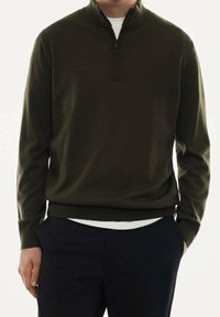 Pull-over vert foncé à quart de zip et col montant, fabriqué dans un matériau lisse et doux, associé à une couche intérieure blanche.