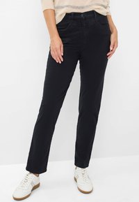 Pantalons noirs à jambe droite avec une texture lisse, dotés de poches avant, d'une fermeture à bouton, et portés avec des baskets blanches.