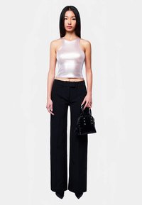 Metallisk sølvfarvet ærmeløs croptop med tætsiddende design, kombineret med højtaljede, sorte bukser med brede ben og en lille sort håndtaske.