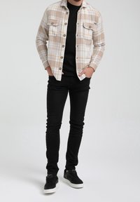 Camicia a quadri beige e bianca con due tasche sul petto, abbinata a jeans skinny neri e sneakers nere. Tessuto dalla consistenza liscia.