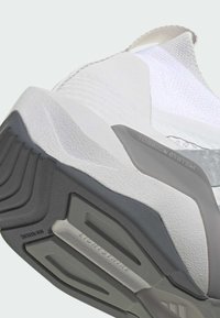 Hvid sportssko med tekstureret overdel, grå sål med multidirektionelle mønstre og 'Torsion System'-branding.