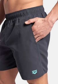 Bañadores de hombre en tejido gris oscuro con cinturilla elástica, bolsillo lateral y costuras y logotipo en azul claro.
