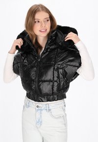 Czarna kurtka puchowa o połyskującej powierzchni, krótki krój, duży kaptur z futrzanym obszyciem i zapięciem na zamek. Lekka z pikowaną teksturą.