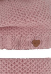 Gebreide roze muts met een gestructureerd patroon, voorzien van een geribbelde rand en een klein metalen hartvormig label met de inscriptie "LOVE".