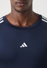 Jūras spēku sporta krekls ar apaļu kakla izgriezumu un īsām piedurknēm. Uz pleciem ir trīs baltas svītras un neliels balts logo uz krūtīm.