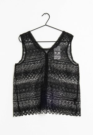 Top in pizzo nero con motivi intricati, caratterizzato da un scollo a barca e orlo ondulato, appeso a un gancio nero su uno sfondo bianco.