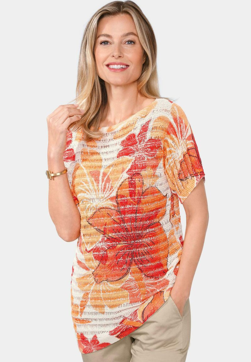 Bluse mit Floralprint, die orange und rote Blumen auf einem strukturierten weißen Hintergrund zeigt; kurze Ärmel und weiter Ausschnitt für eine lässige Passform.