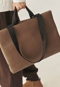 Bruine vegan leren shopper met geperst ontwerp, zwarte stoffen handvatten, rechthoekige vorm en gladde textuur.