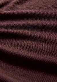 Detail náhľadu na mäkkú, ribbovanú tkaninu v tmavofialovej farbe s jemnými záhybmi, ktoré vytvárajú variácie svetla a tieňa.