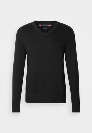 Pull noir en tricot avec un col en V. Il dispose de manches longues et d'un petit logo sur la poitrine. Texture lisse.