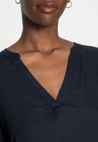 Haut bleu marine à col en V en tissu doux, avec un léger détail froncé au niveau de l'encolure et une silhouette décontractée avec des manches courtes.