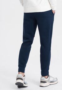 Marina blå sweatpants i mjukt tyg med ribbade muddarmar och sidofickor, tillsammans med grå träningsskor med ljusa detaljer.