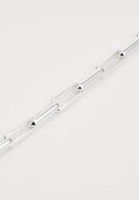 Chaîne en métal argenté avec des maillons allongés en forme d'ovale. Surface lisse avec un fini poli et un design sans couture, réfléchissant la lumière.