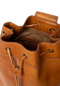 Tan läder bucket-väska med texturerad yta, öppen topp, snörning och kontrasterande vit sömnad. Inre ficka synlig.