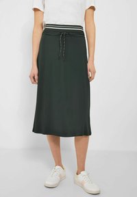 Mørkegrøn midi-nederdel med elastisk talje, snøre og hvide stribede detaljer; bæres med hvide sneakers for et afslappet look.