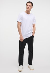 Camiseta blanca de algodón con cuello redondo, combinada con pantalones negros y zapatillas blancas. Diseño sencillo, textura suave y corte regular.