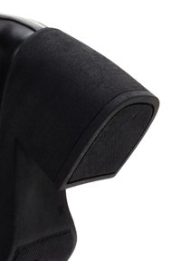 Zapato de tacón alto negro con un upper de tela texturizada y un acento de cuero suave. El tacón tiene una forma geométrica y suela de goma.