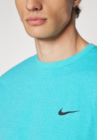 T-shirt en coton turquoise avec un col rond, présentant un accent en logo Nike noir sur la poitrine et une texture lisse.