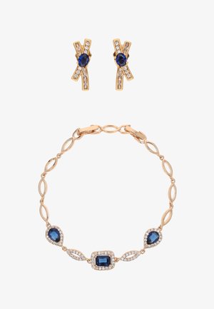 Sieradenset in goudkleur met een armband met ovale schakels en blauwe stenen, samen met bijpassende oorbellen met blauwe centrale stenen en heldere accenten.