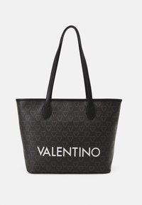 Black tote bag with textured fabric, featuring a repeating triangular pattern. A prominent white “VALENTINO” logo printed on the front.