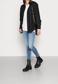 Camicia nera oversize, maglione bianco, jeans skinny blu chiaro e stivaletti neri con suola spessa. Design semplice, senza motivi o dettagli visibili.