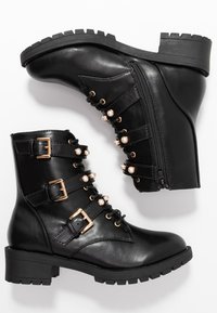 Černé kotníkové boty z umělé kůže s robustním podpatkem, předním šněrováním, zlatými detaily a dekoračními umělými perlami na páscích. Boční zip.