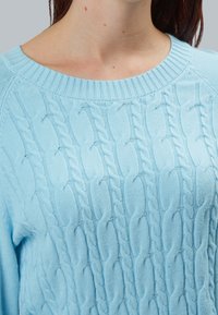Maglione azzurro chiaro a maglia con un collo a coste e un motivo testurizzato, realizzato in un morbido tessuto lavorato a maglia. Primo piano del collo e del design.