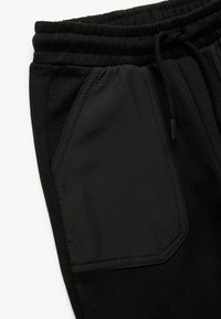 Zwarte joggers met een trekkoord in de taille, een zachte textuur en een contrasterend glad zakpaneel met decoratieve stiksels.