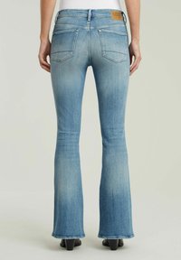 Fitted flared jeans i blått med en sliten textur, med två bakfickor och en brun läderlapp vid midjan.