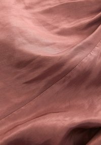 Mäkká, textúrovaná látka v ružovej farbe, s jemnými záhybmi a hladkým povrchom s subtílnym leskom.