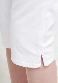 Valkoiset puuvillashortsit suoralinjaisella leikkauksella, joissa on sivureikä helman kohdalla ja siisti ompelus. Pehmeä rakenne.