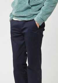 Marineblauwe broek met een gladde textuur, voorzien van zijzakken en een recht gesneden ontwerp, gecombineerd met een zachte turquoise fleece hoodie.