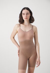 Bruine naadloze bodysuit met verstelbare bandjes, textuurdesign en lengte tot halverwege de bovenbenen. Gemaakt van rekbaar materiaal voor comfort.