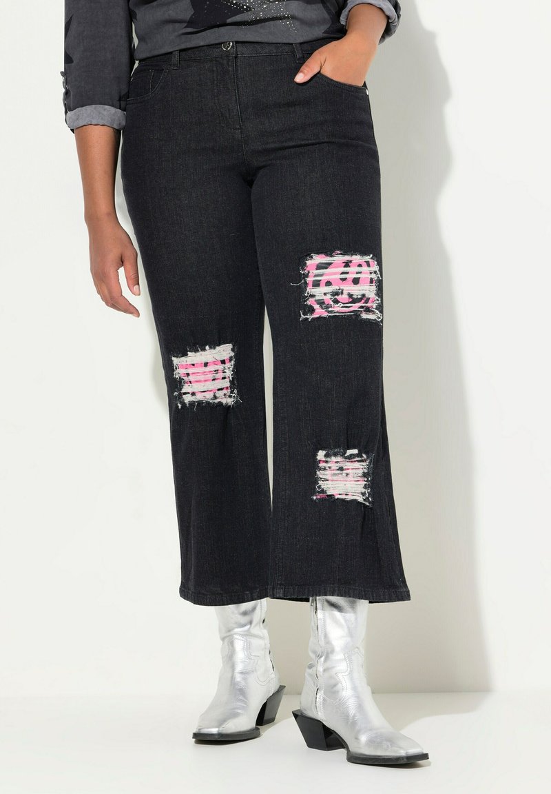 Jeans neri a gamba larga con toppe strappate che rivelano un tessuto a righe rosa e bianca, abbinati a stivaletti argento. Tessuto denim testurizzato.